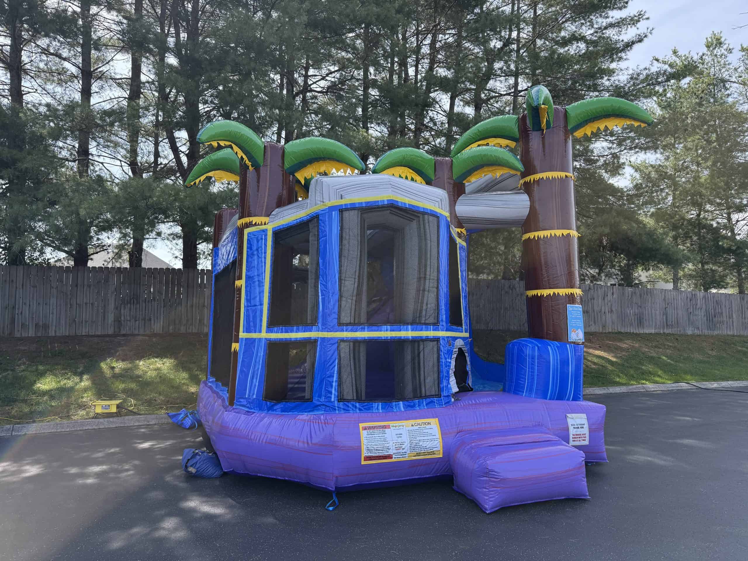 Inflatable bounce house with tropical treehouse design, palm trees, and vibrant colors for kids' par.