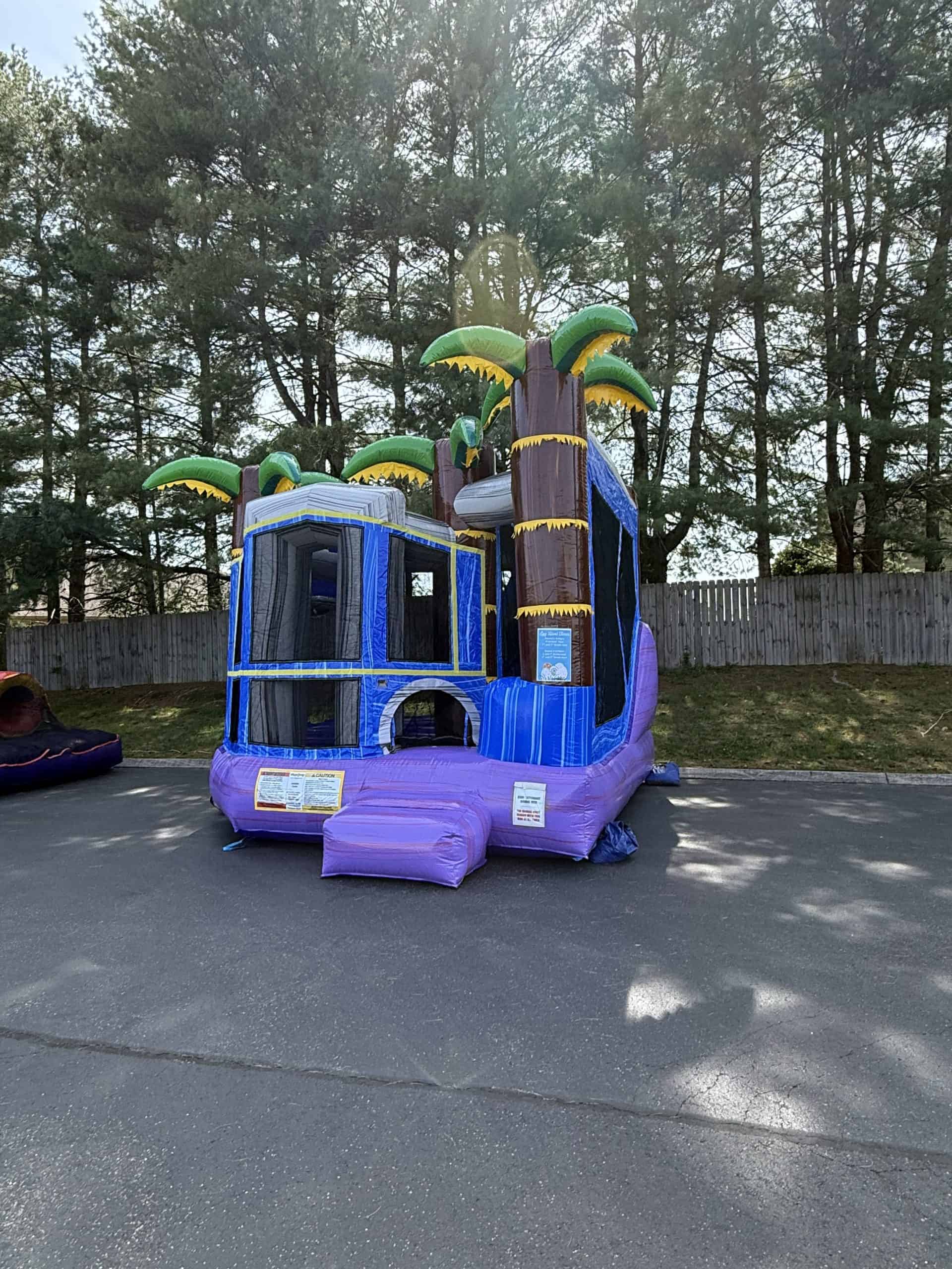 Inflatable jungle-themed bounce house with slides and palm trees for children's parties.